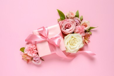 Gift box and beautiful flowers on pink background, flat lay