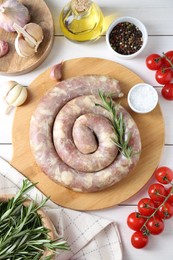 Raw homemade sausage, spices and other products on white wooden table, flat lay