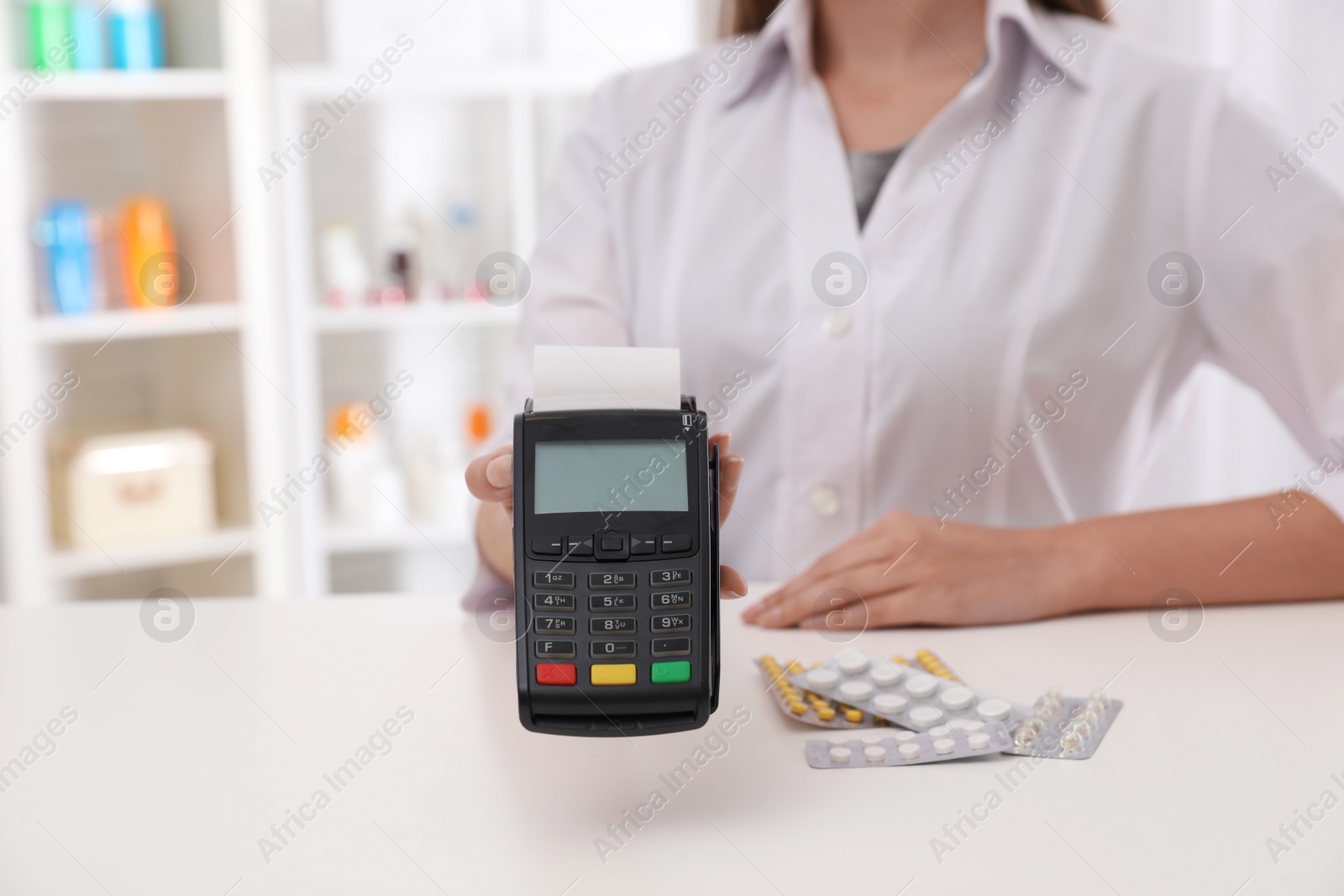 Photo of Pharmacist with payment terminal and pills in drug store, closeup. Space for text