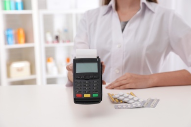 Pharmacist with payment terminal and pills in drug store, closeup. Space for text