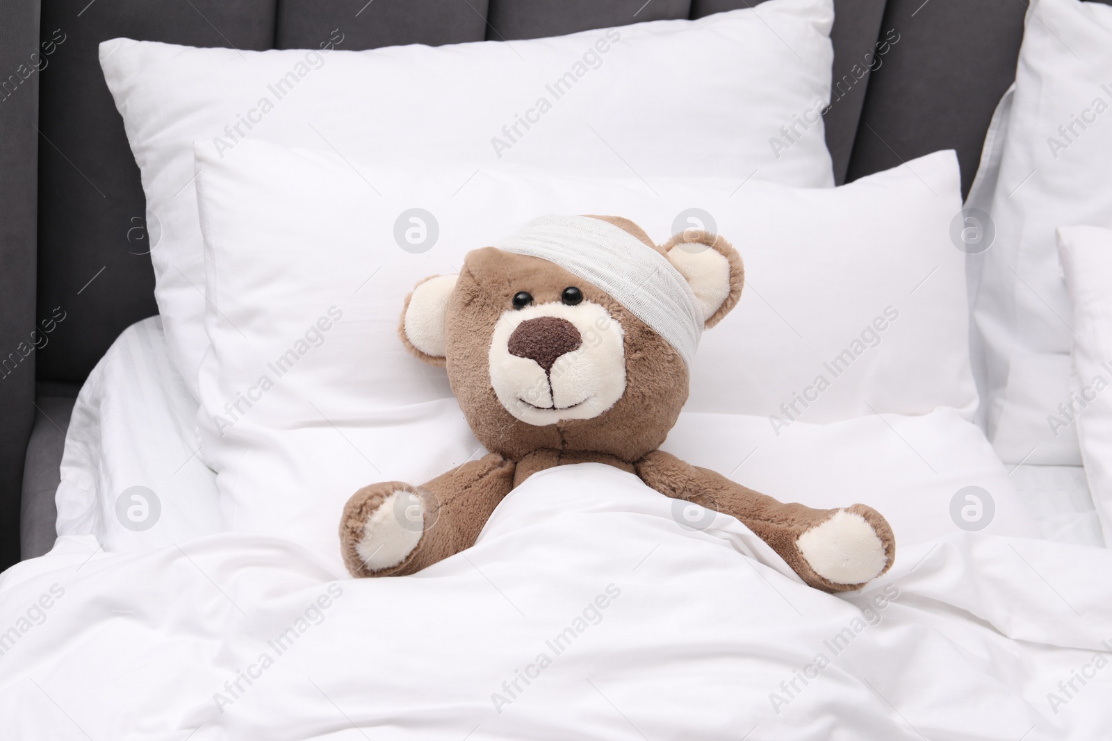 Photo of Toy cute bear with bandage under blanket in bed