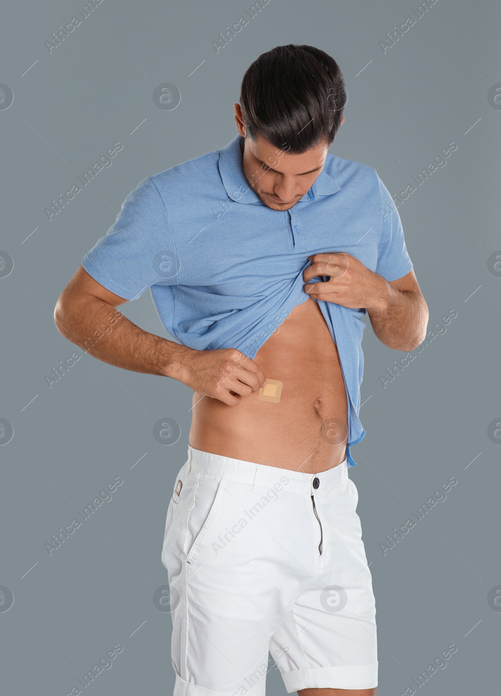 Photo of Man putting sticking plaster onto tummy against light grey background