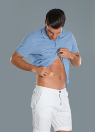 Photo of Man putting sticking plaster onto tummy against light grey background