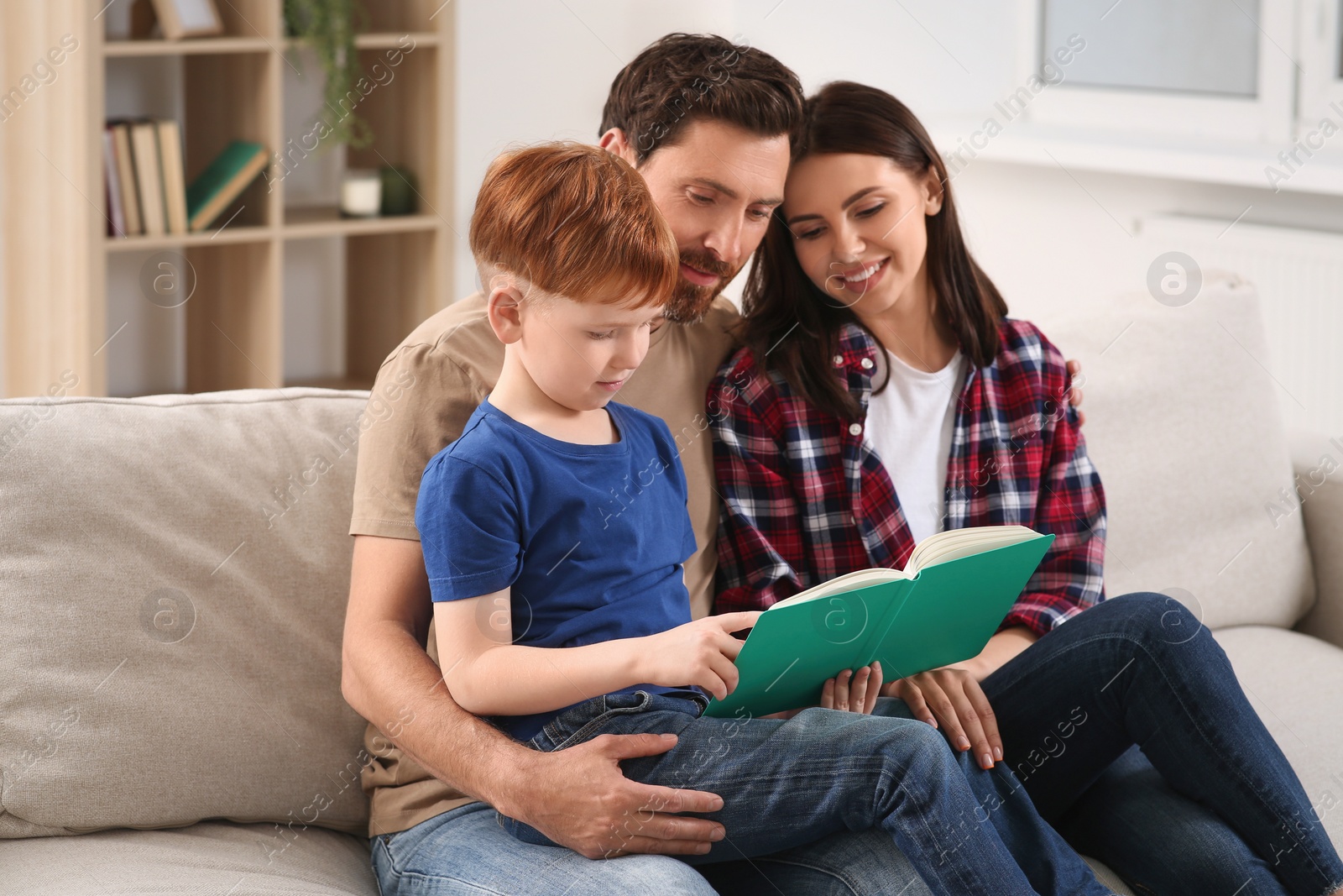 Photo of Happy parents with their child reading book on couch at home