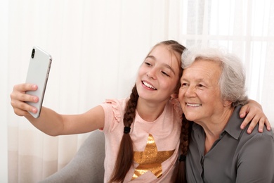 Photo of Happy cute girl taking selfie with her grandmother at home