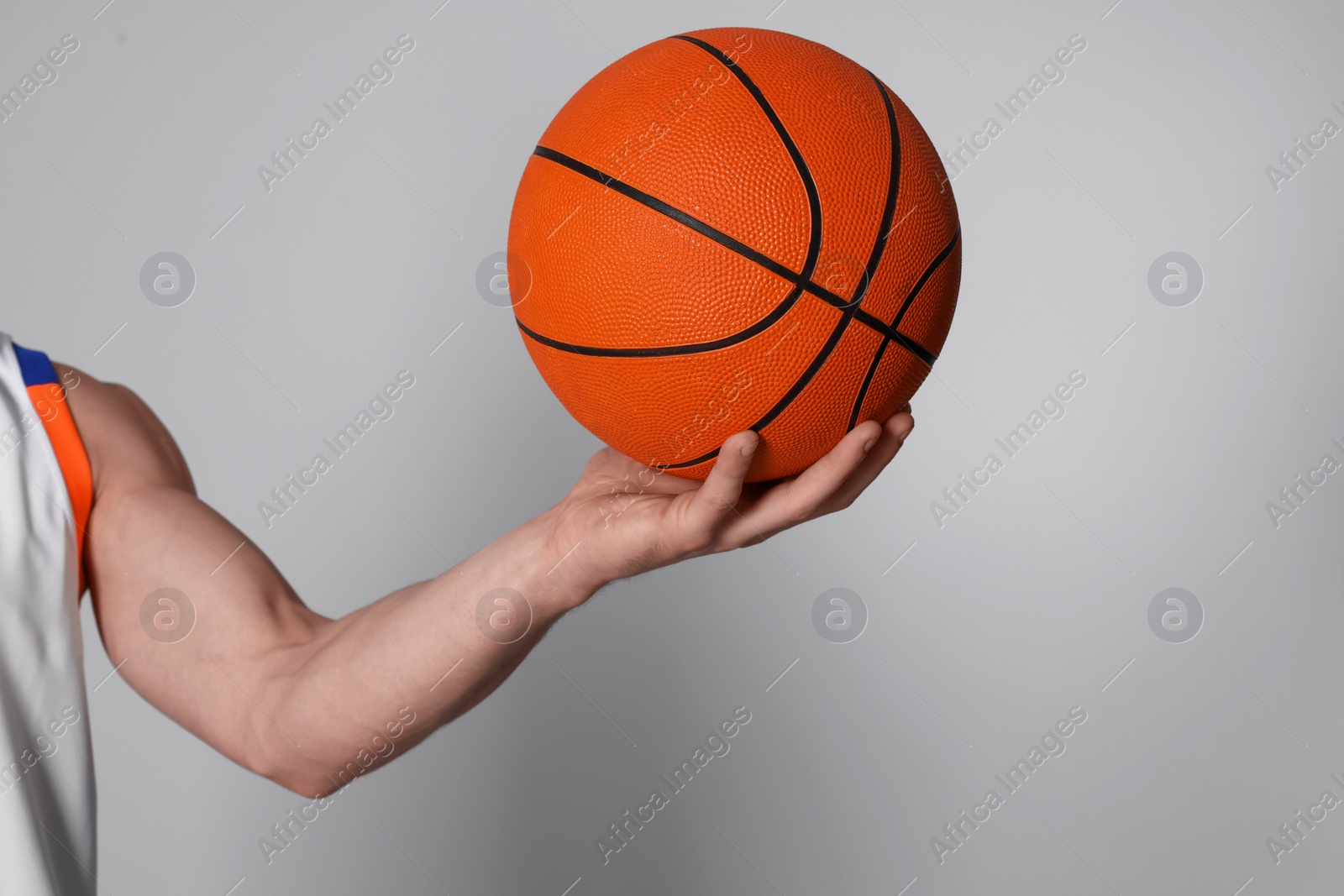 Photo of Athletic young man with basketball ball on light grey background, closeup. Space for text