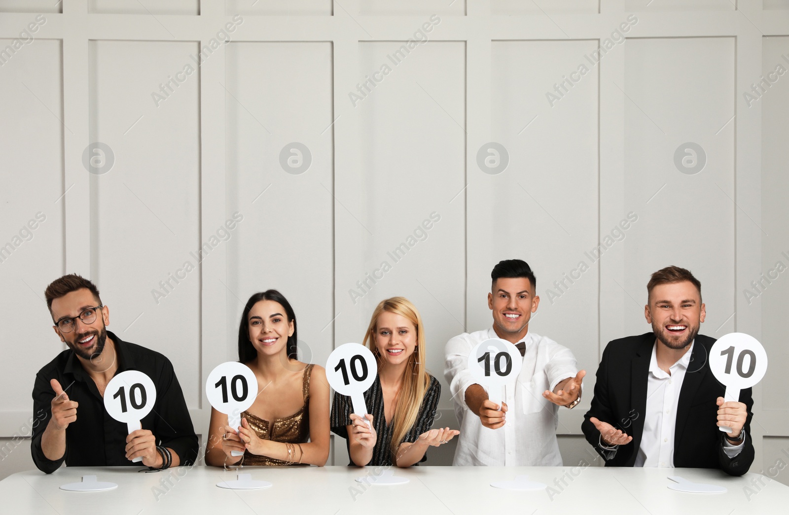 Photo of Panel of judges holding signs with highest score at table against light wall