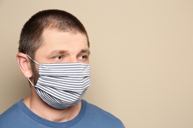 Photo of Man wearing handmade cloth mask on beige background, space for text. Personal protective equipment during COVID-19 pandemic