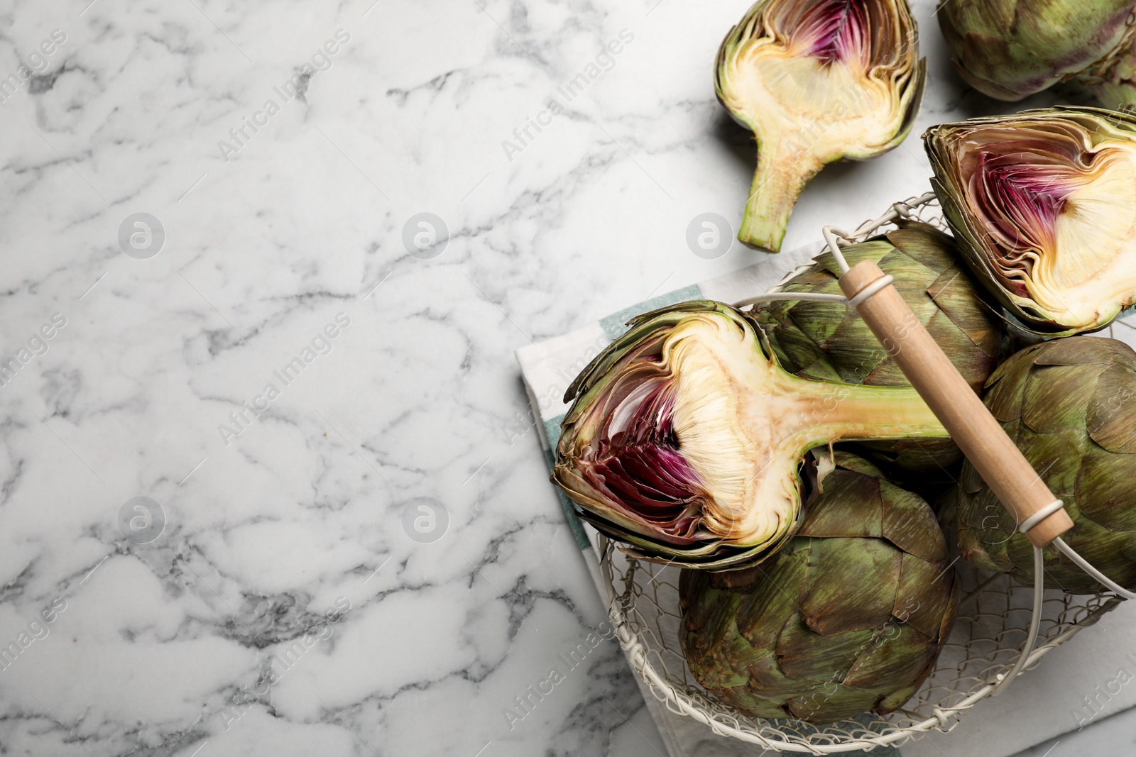 Photo of Cut and whole fresh raw artichokes on white marble table, flat lay. Space for text