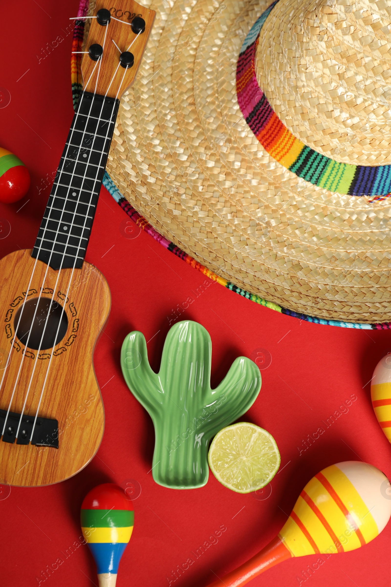 Photo of Flat lay composition with Mexican sombrero hat and ukulele on red background