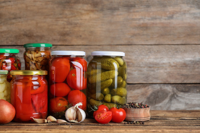 Photo of Glass jars with different pickled vegetables on wooden table