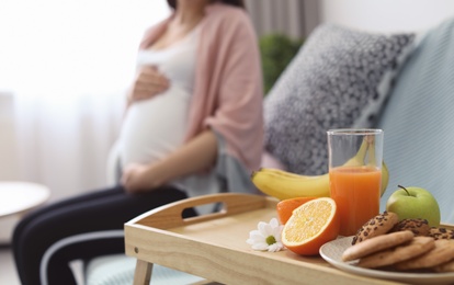 Photo of Tray with fresh fruits, cookies and pregnant woman on background