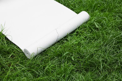 Photo of White karemat or fitness mat on green grass outdoors. Space for text