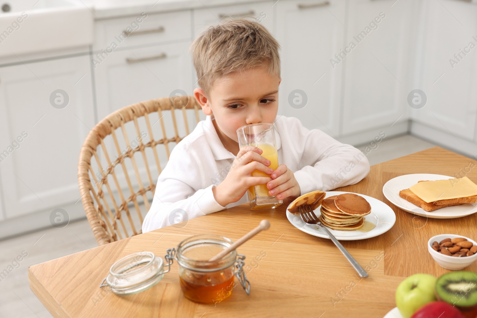 Photo of Breakfast time. Cute little boy drinking juice at table in kitchen