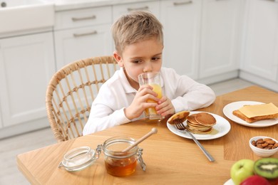 Breakfast time. Cute little boy drinking juice at table in kitchen