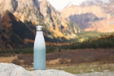 Thermo bottle on rock in mountains. Space for text