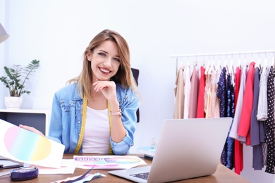 Photo of Beautiful young stylist at workplace near rack with clothes