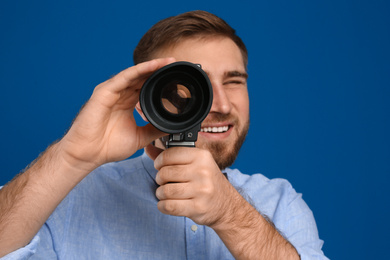 Young man using vintage video camera on blue background, focus on lens