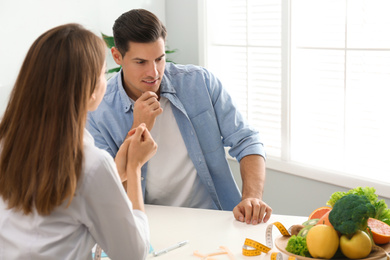 Young nutritionist consulting patient at table in clinic