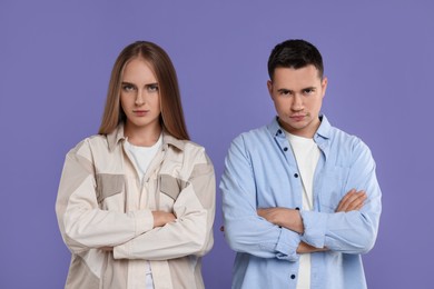 Portrait of resentful couple with crossed arms on violet background
