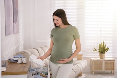 Photo of Pregnant woman holding baby diapers at home