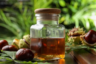 Photo of Chestnuts, leaves and jar of essential oil on table against blurred background