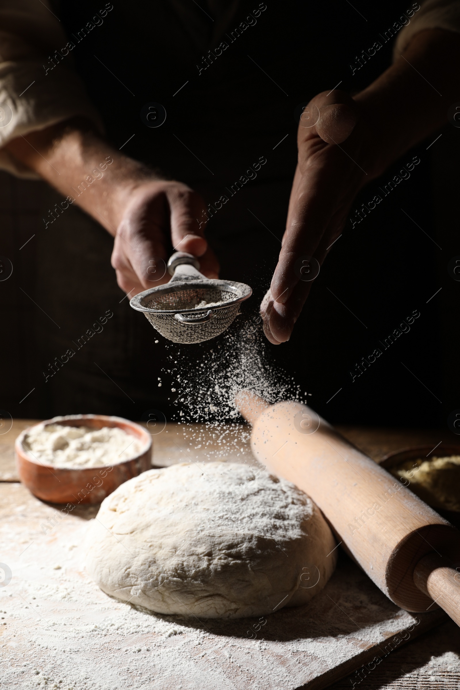 Photo of Man sprinkling flour over dough at wooden table, closeup