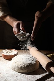 Man sprinkling flour over dough at wooden table, closeup