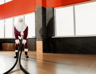 Young Santa Claus training with ropes in modern gym