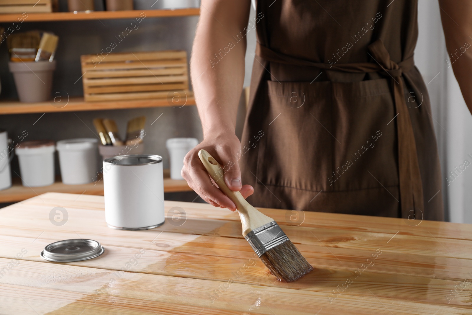 Photo of Man varnishing wooden surface with brush indoors, closeup