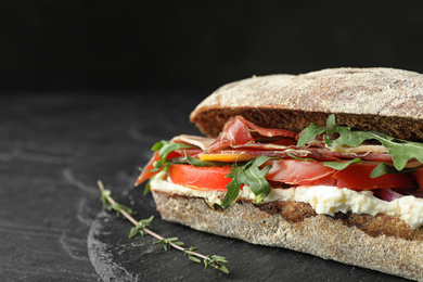 Delicious sandwich with fresh vegetables and prosciutto on black table, closeup. Space for text