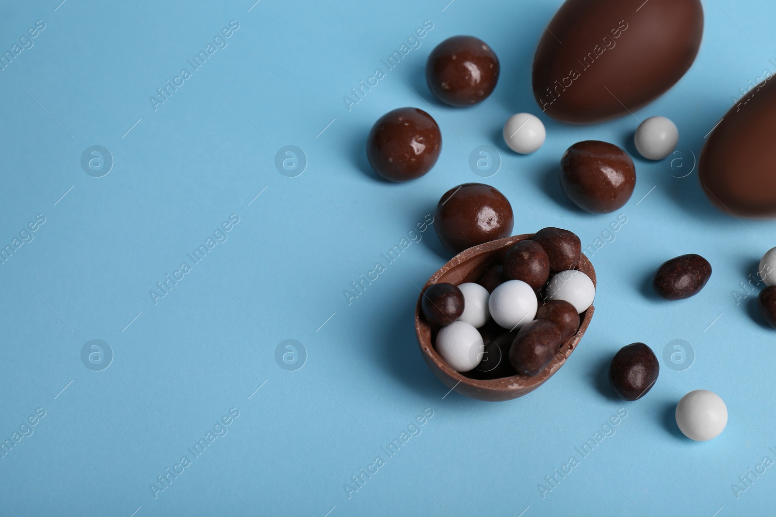 Photo of Tasty chocolate eggs and different sweets on light blue background, above view. Space for text