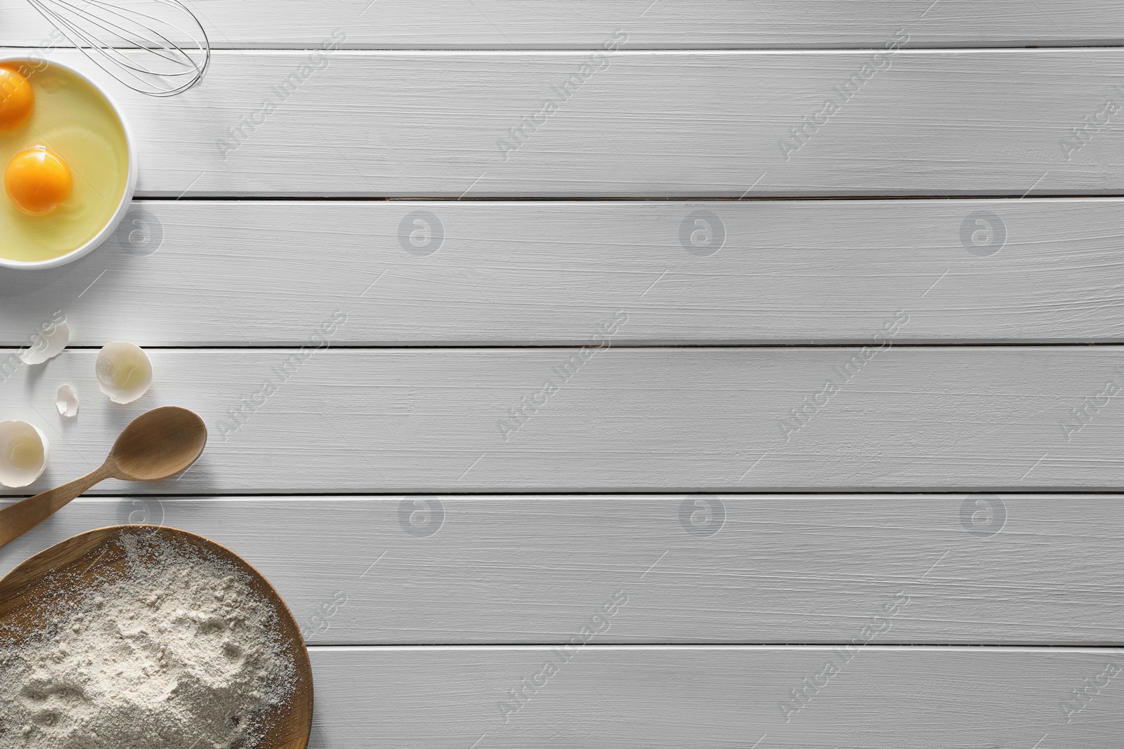 Photo of Food photography. Yolks, eggshell, spoon, flour and whisk on white wooden table, flat lay with space for text