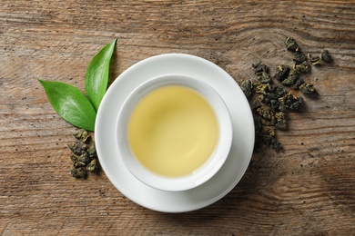 Photo of Cup of Tie Guan Yin oolong and tea leaves on wooden table, top view