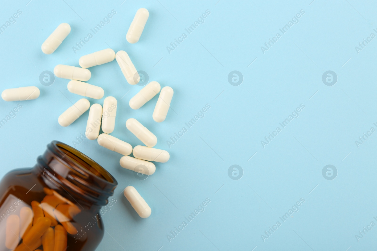 Photo of Bottle and vitamin capsules on light blue background, top view. Space for text