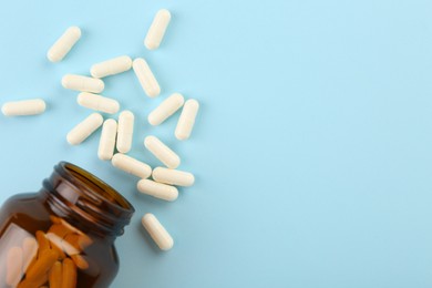 Bottle and vitamin capsules on light blue background, top view. Space for text