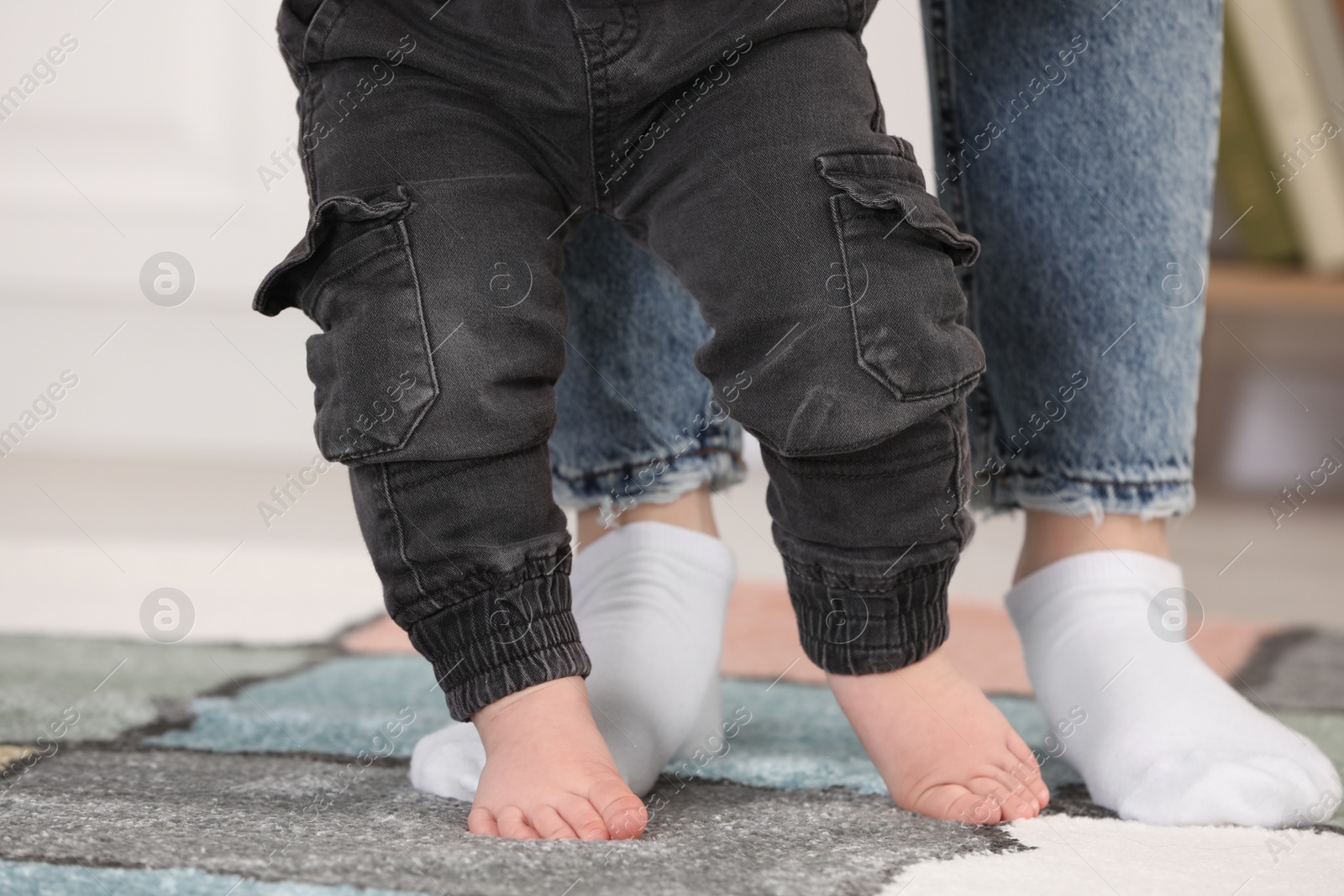 Photo of Mother supporting her son while he learning to walk on carpet indoors, closeup