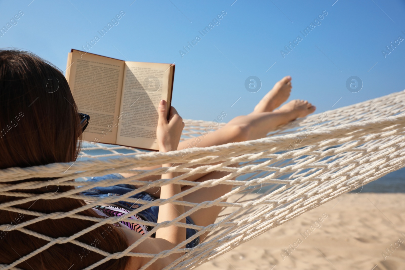 Photo of Young woman reading book in hammock on beach