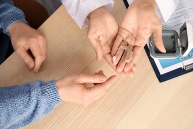 Photo of Doctor giving patient hearing aid at table in clinic, closeup