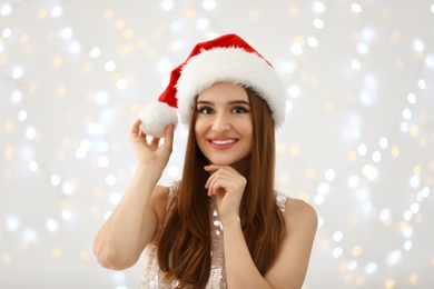 Happy young woman in Santa hat against blurred Christmas lights