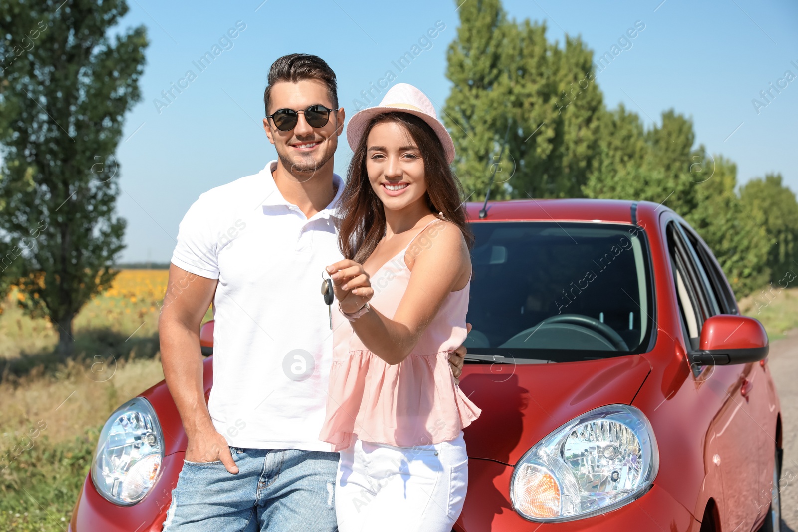 Photo of Happy young couple with key standing near new car on road