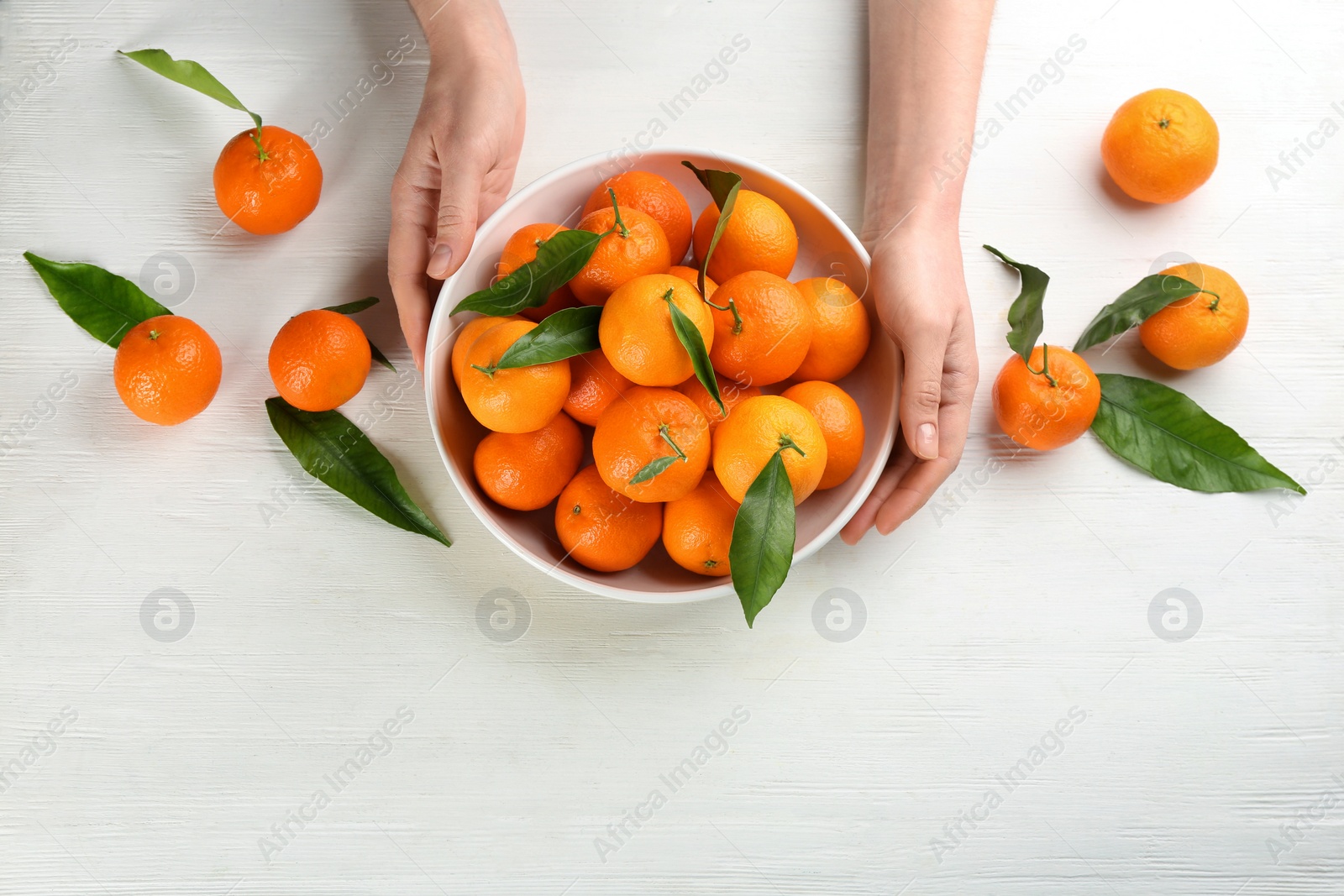 Photo of Woman with fresh ripe tangerines at white wooden table, top view