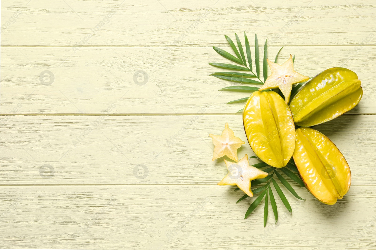 Photo of Delicious carambola fruits on yellow wooden table, flat lay. Space for text