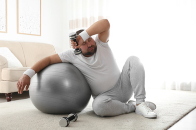 Lazy overweight man with sport equipment on floor at home