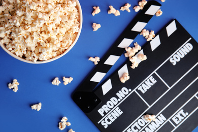 Photo of Tasty pop corn and clapboard on blue background, flat lay