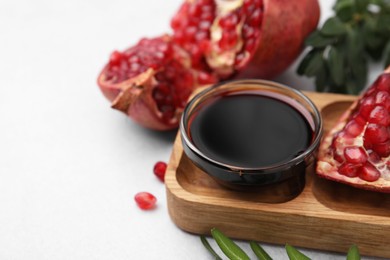 Photo of Tasty pomegranate sauce in bowl, branches and fruits on light table, closeup. Space for text