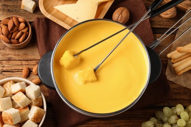 Pot of tasty cheese fondue and snacks on wooden table, flat lay