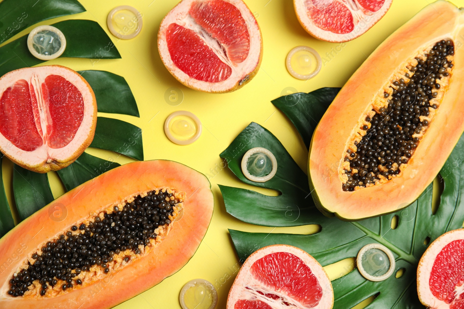 Photo of Flat lay composition with condoms and exotic fruits on yellow background. Erotic concept