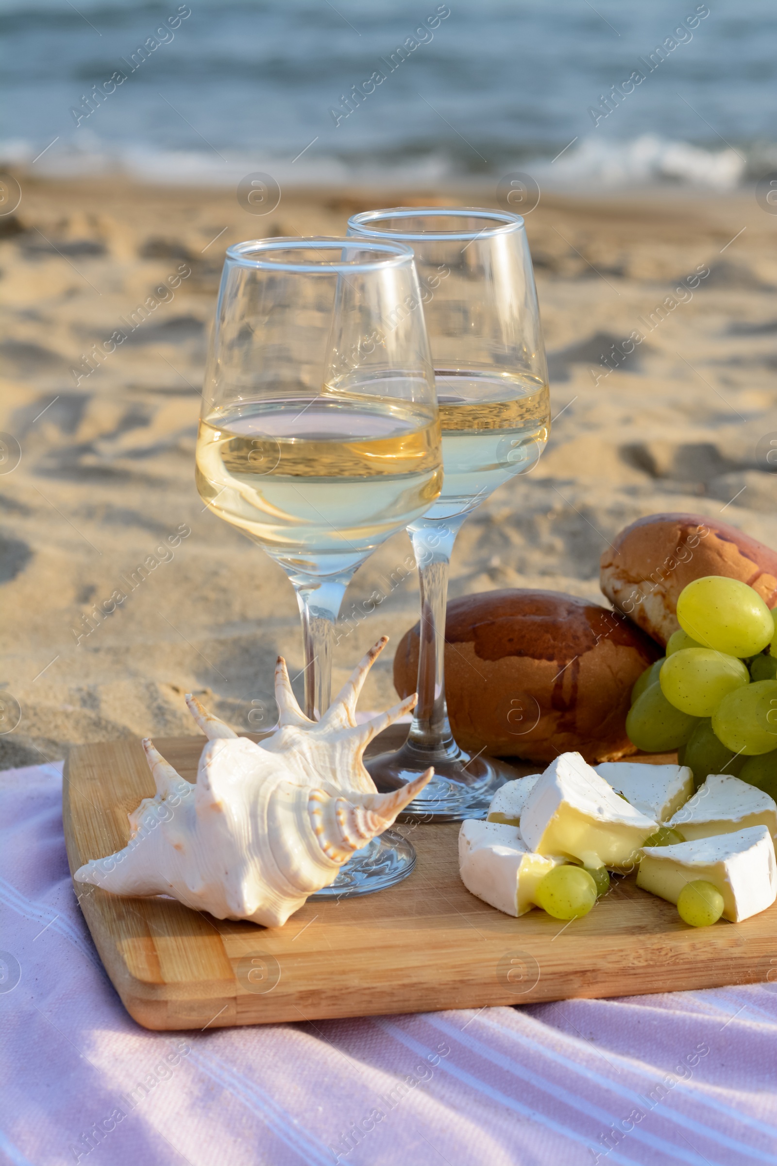 Photo of Glasses with white wine and snacks for beach picnic on sandy seashore