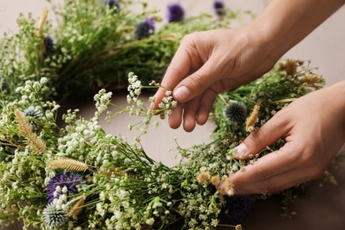Photo of Woman making beautiful wreath of wildflowers at wooden table, closeup